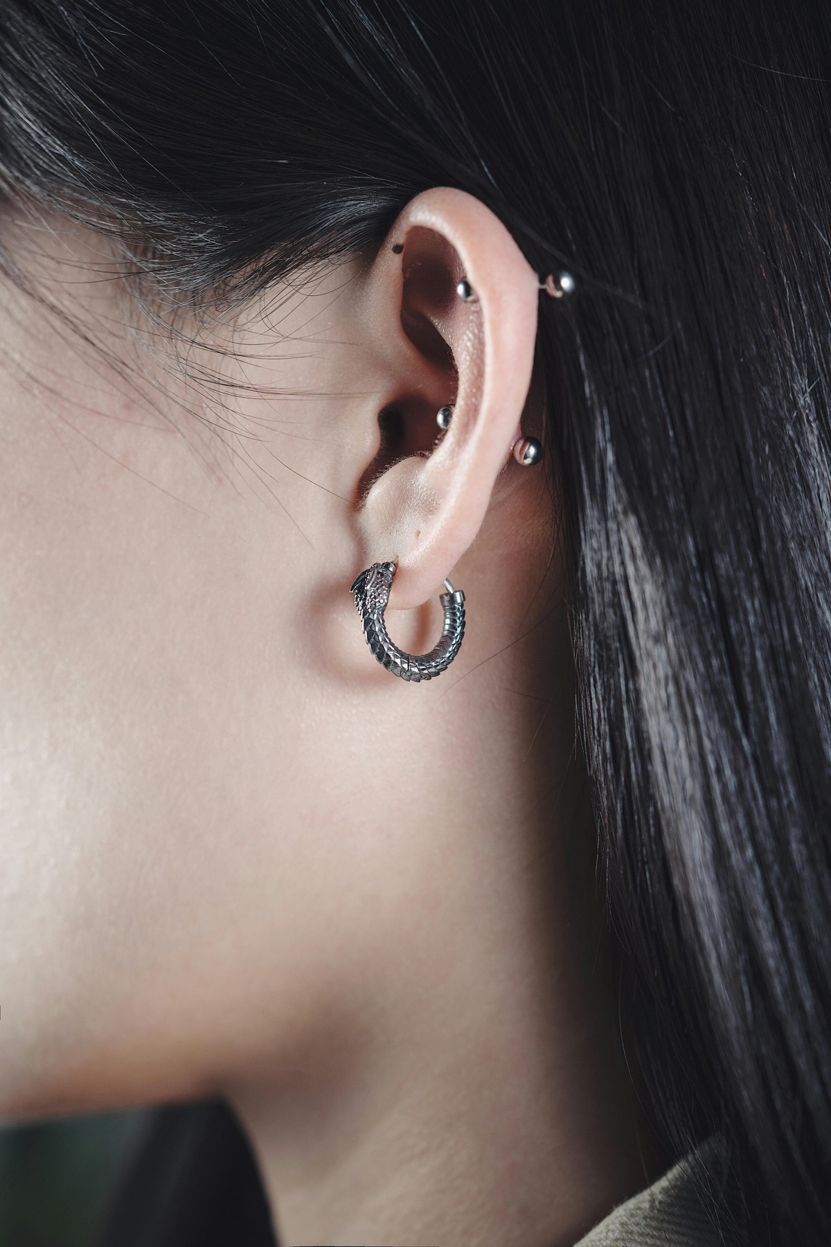 Close-up of an ear with multiple helix piercings and a snake hoop earring