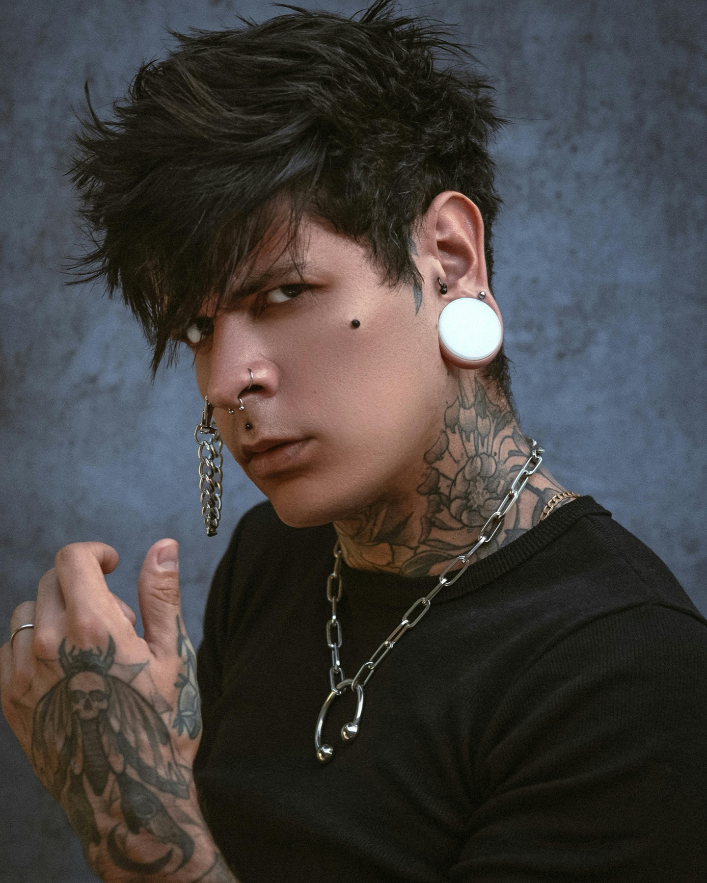 Green-lit portrait with sunglasses, a lip piercing, and layered jewelry