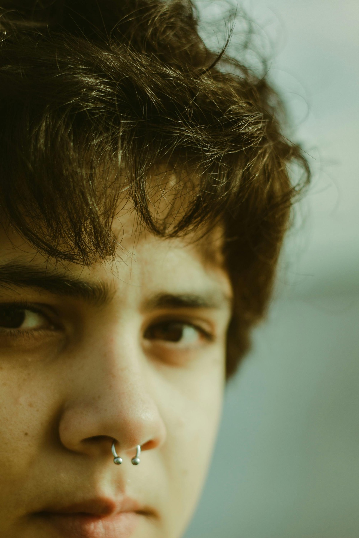 Close portrait with a silver septum ring in green-toned light